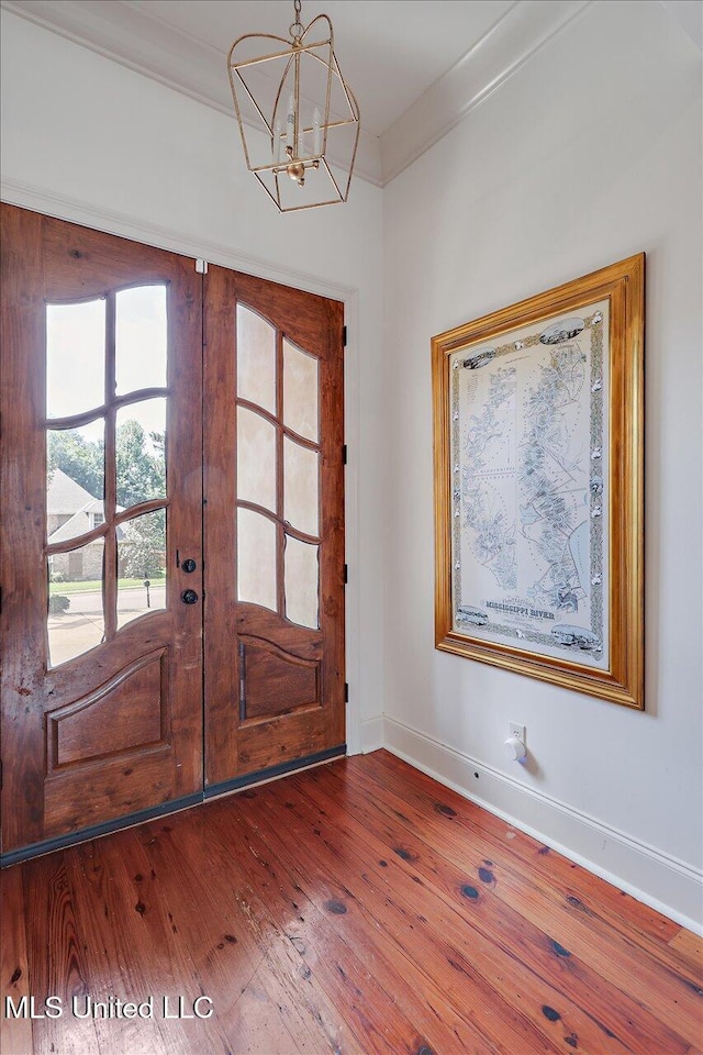 foyer entrance featuring french doors, crown molding, baseboards, wood-type flooring, and an inviting chandelier