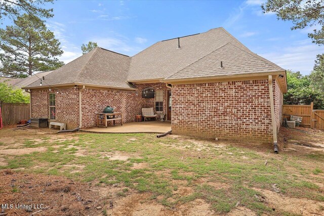 back of house featuring brick siding, fence, a shingled roof, and a patio area