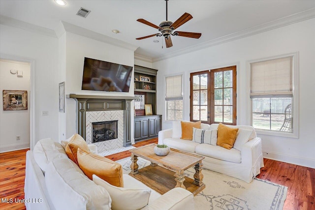 living room featuring crown molding, visible vents, baseboards, a ceiling fan, and light wood finished floors
