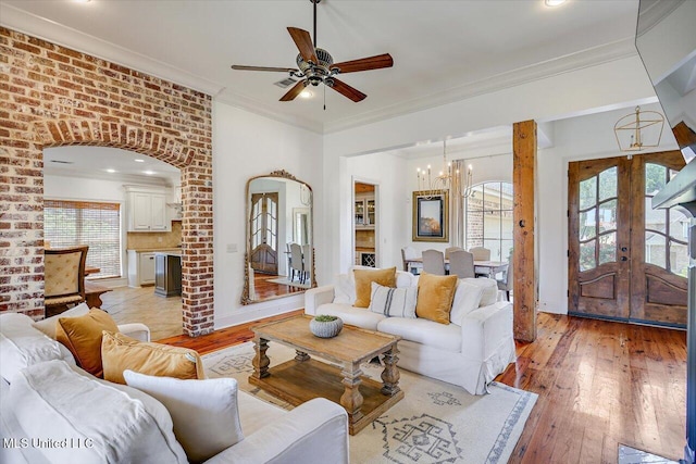 living area with light wood-style flooring, ornamental molding, a healthy amount of sunlight, and ceiling fan with notable chandelier