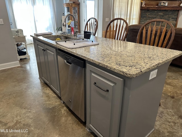 kitchen featuring stainless steel dishwasher, light stone counters, gray cabinetry, sink, and a center island with sink