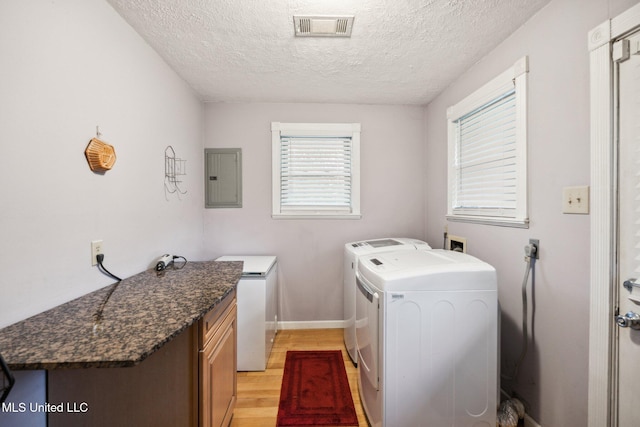 washroom featuring electric panel, a textured ceiling, light hardwood / wood-style flooring, and washing machine and clothes dryer