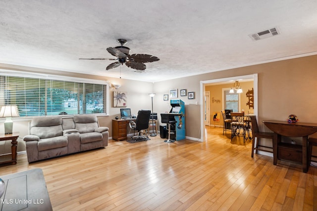 living room with ceiling fan with notable chandelier, a textured ceiling, light wood-type flooring, and crown molding