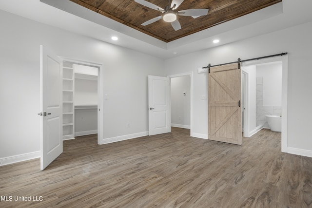 unfurnished bedroom with wood ceiling, a tray ceiling, wood-type flooring, a spacious closet, and a barn door