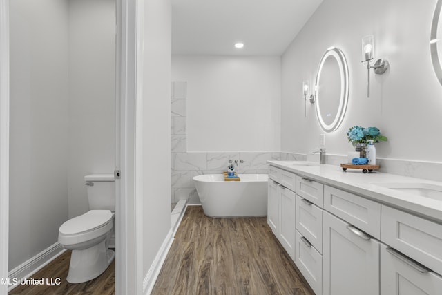 bathroom featuring toilet, tile walls, vanity, hardwood / wood-style floors, and a washtub