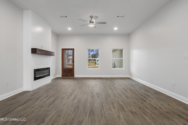 unfurnished living room featuring heating unit, dark wood-type flooring, a large fireplace, and ceiling fan