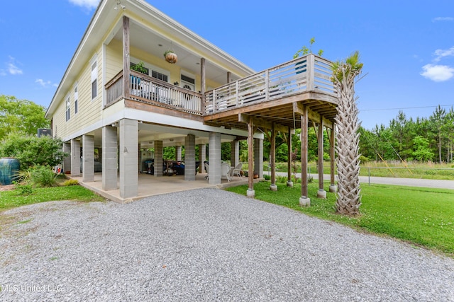 back of property featuring a deck, a patio, driveway, a lawn, and a carport