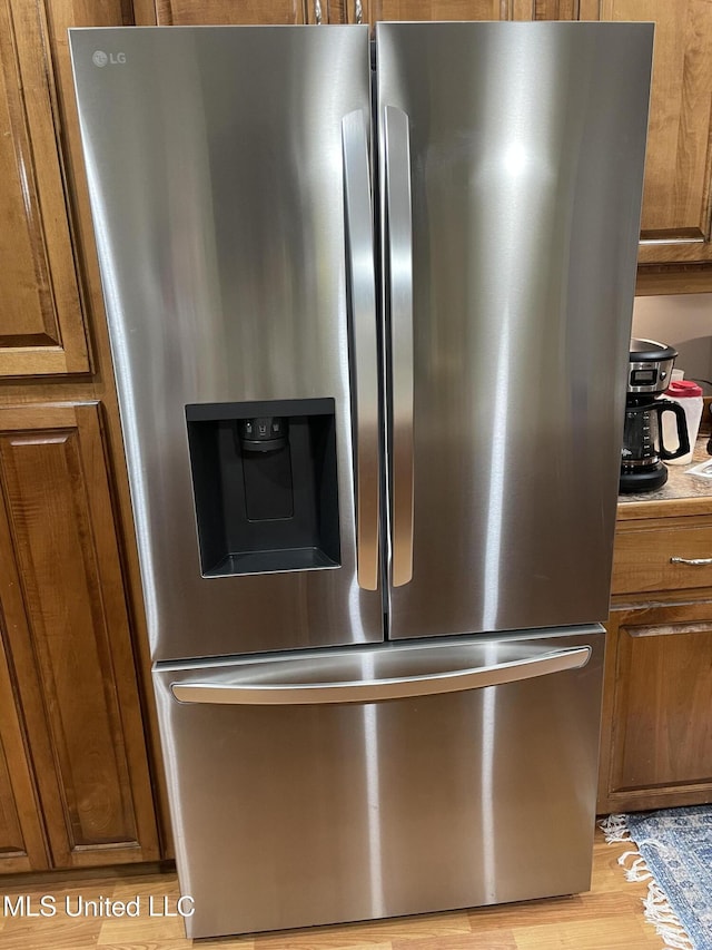 room details featuring light countertops, light wood-type flooring, brown cabinets, and stainless steel fridge with ice dispenser