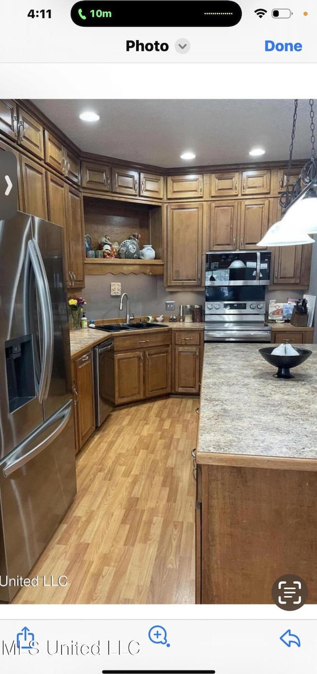 kitchen with light wood finished floors, stainless steel appliances, light countertops, open shelves, and a sink