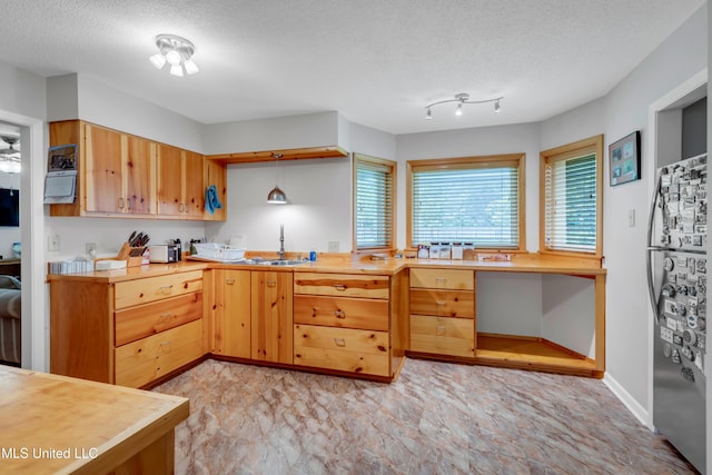kitchen with a sink, freestanding refrigerator, a textured ceiling, and light countertops
