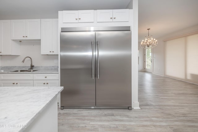 kitchen featuring light wood-style flooring, light stone counters, white cabinetry, a sink, and built in fridge