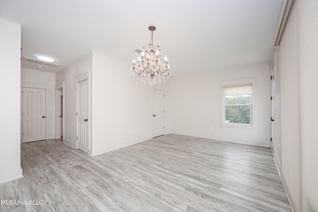 spare room with light wood finished floors, baseboards, and an inviting chandelier