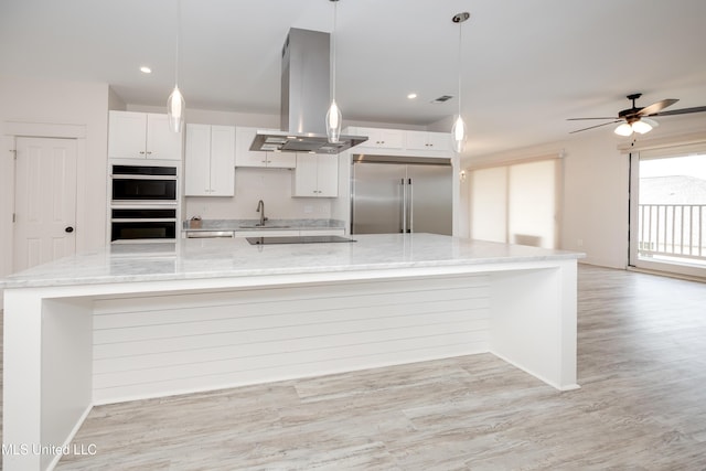 kitchen with island exhaust hood, multiple ovens, stainless steel built in refrigerator, white cabinetry, and a sink