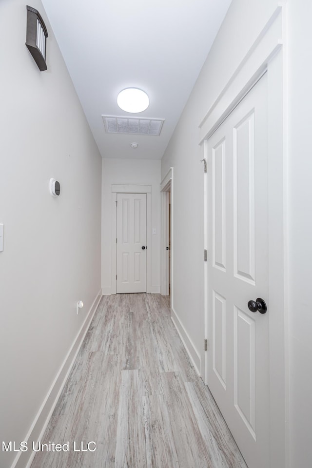 hallway with light wood-style floors, visible vents, and baseboards