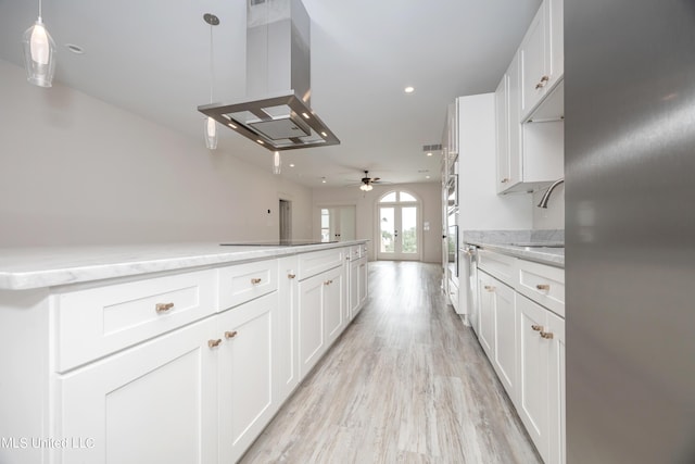 kitchen with sink, ceiling fan, decorative light fixtures, island range hood, and white cabinetry