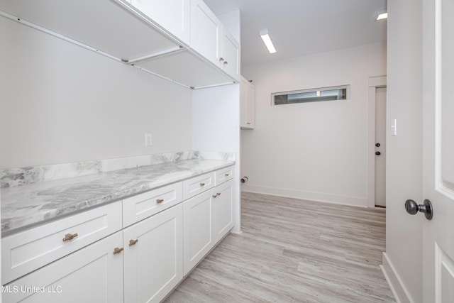 kitchen with light wood-style flooring, baseboards, white cabinets, and light stone counters