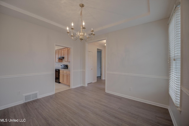 unfurnished dining area with a tray ceiling, a chandelier, and light hardwood / wood-style flooring