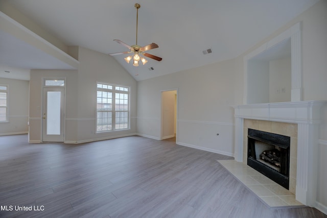 unfurnished living room featuring ceiling fan, plenty of natural light, a tiled fireplace, and light hardwood / wood-style flooring