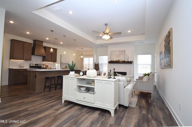 living room featuring dark wood-type flooring, plenty of natural light, a raised ceiling, and ceiling fan with notable chandelier