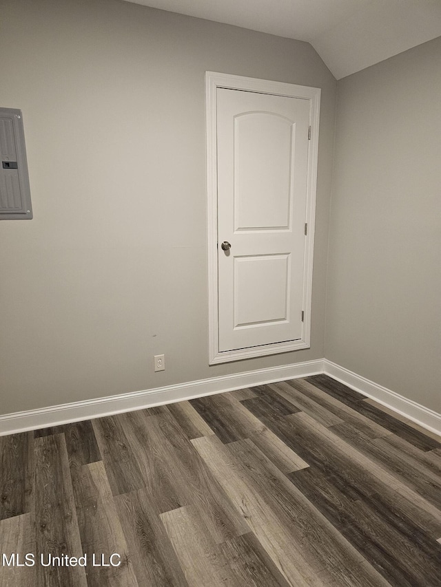 spare room featuring electric panel, dark wood-style floors, baseboards, and vaulted ceiling