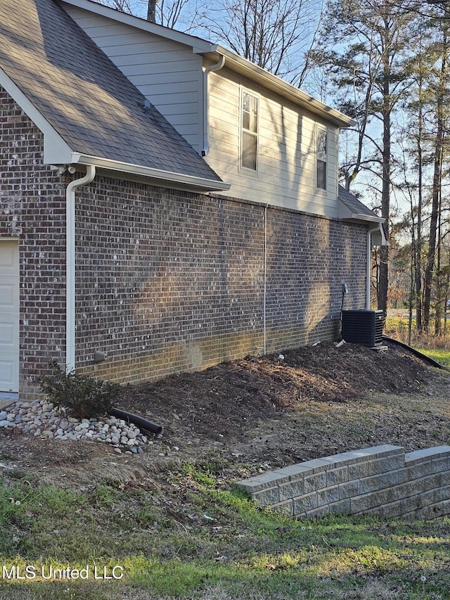 view of home's exterior featuring brick siding, central air condition unit, an attached garage, and a shingled roof