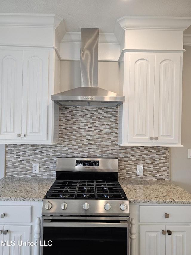 kitchen with gas range, white cabinetry, wall chimney range hood, and ornamental molding