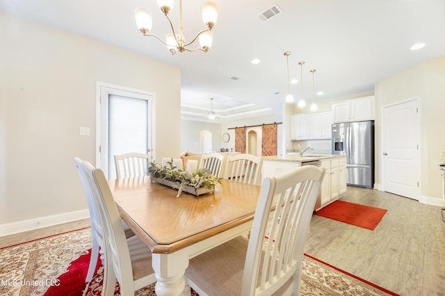 dining room featuring light wood-type flooring, visible vents, baseboards, and a raised ceiling