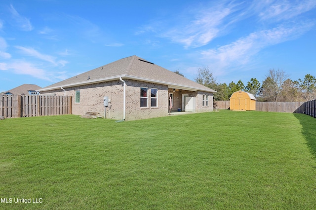 back of house with an outbuilding, a fenced backyard, brick siding, a lawn, and a storage unit