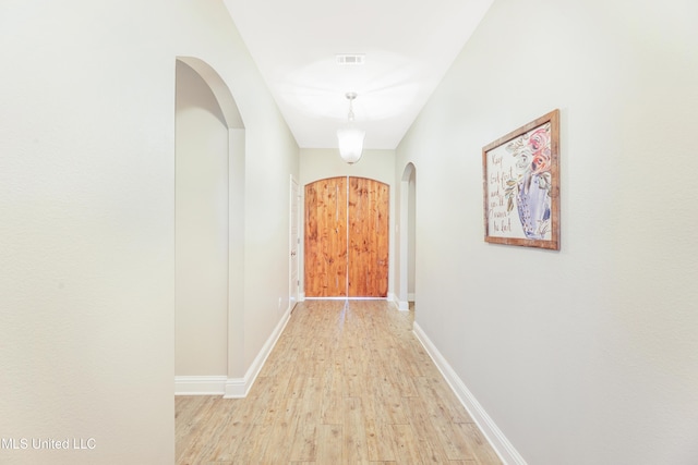 hallway with arched walkways, light wood-type flooring, visible vents, and baseboards