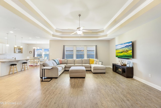 living area with light wood-type flooring, baseboards, a raised ceiling, and crown molding