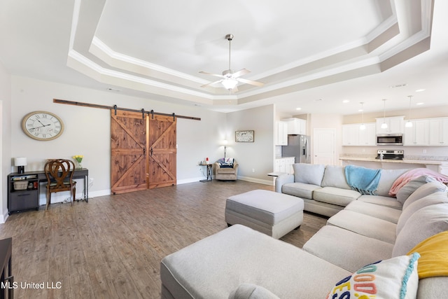 living room featuring wood finished floors, a barn door, a raised ceiling, and crown molding