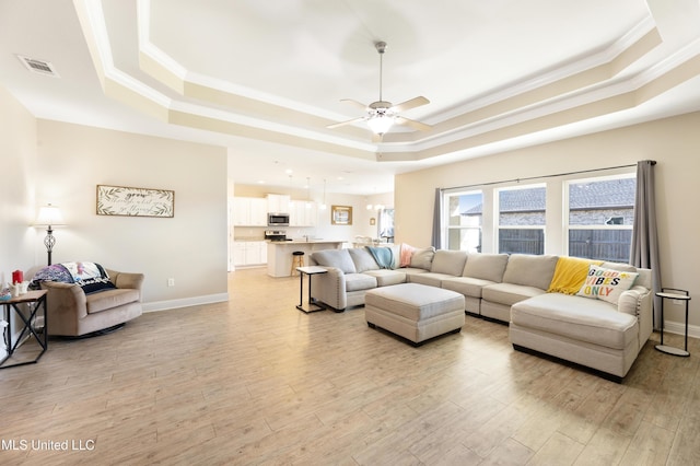 living room featuring light wood-type flooring, visible vents, a raised ceiling, and ornamental molding