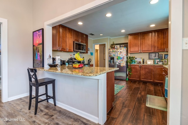 kitchen with dark wood-type flooring, a kitchen breakfast bar, kitchen peninsula, appliances with stainless steel finishes, and light stone counters