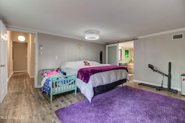 bedroom featuring crown molding, a barn door, hardwood / wood-style flooring, and connected bathroom