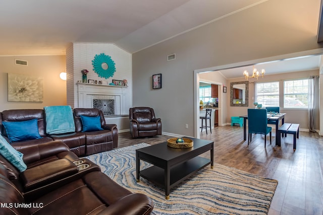 living room featuring lofted ceiling, a notable chandelier, hardwood / wood-style flooring, and a brick fireplace