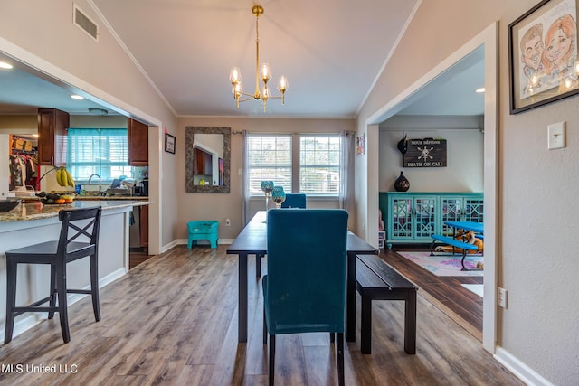 dining room with ornamental molding, vaulted ceiling, a notable chandelier, and hardwood / wood-style flooring