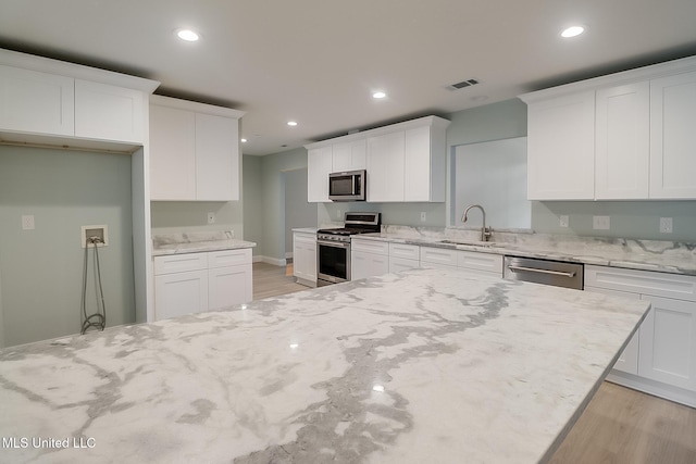 kitchen featuring white cabinets, sink, light stone countertops, light wood-type flooring, and stainless steel appliances