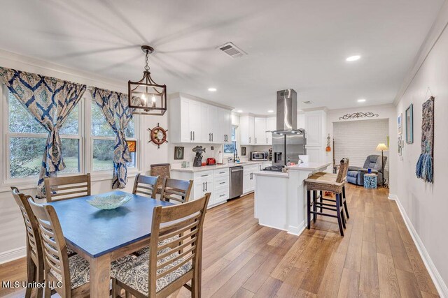 dining space featuring light wood-type flooring, a notable chandelier, crown molding, and sink