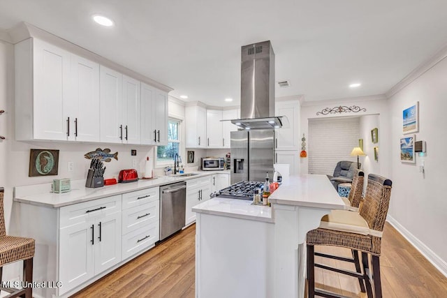 kitchen featuring appliances with stainless steel finishes, white cabinetry, island range hood, and a breakfast bar area