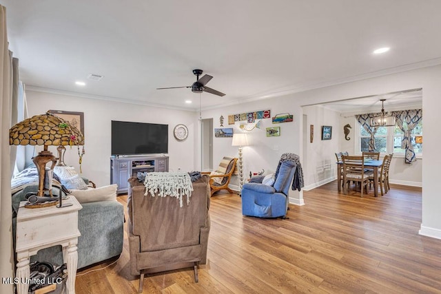 living room with ceiling fan with notable chandelier, light wood-type flooring, and ornamental molding