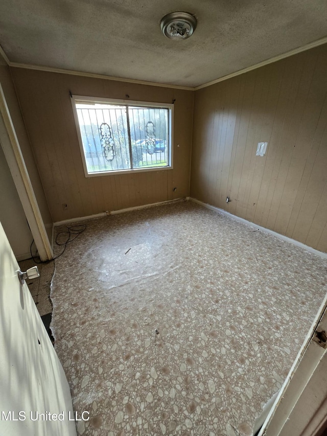 spare room with wooden walls, a textured ceiling, and ornamental molding