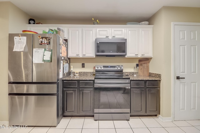 kitchen featuring white cabinets, light tile patterned floors, stainless steel appliances, and dark stone counters