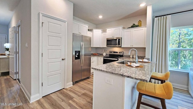 kitchen featuring a breakfast bar area, kitchen peninsula, stainless steel appliances, light stone countertops, and white cabinets