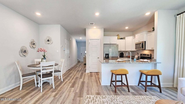 kitchen with light wood-type flooring, kitchen peninsula, stainless steel appliances, white cabinets, and light stone counters