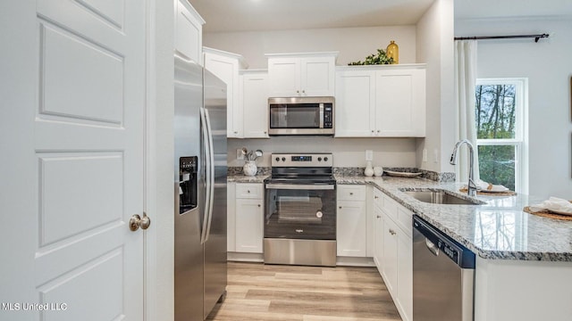 kitchen with stainless steel appliances, sink, light stone countertops, light wood-type flooring, and white cabinetry