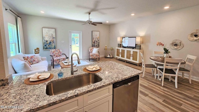 kitchen with sink, light wood-type flooring, stainless steel dishwasher, white cabinets, and light stone counters