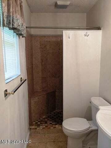 bathroom with a tile shower, a textured ceiling, and toilet