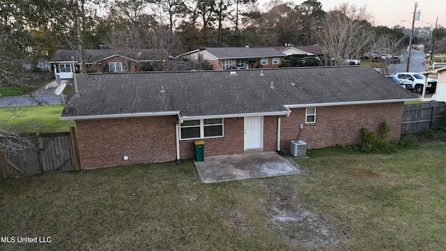 back house at dusk with a yard, a patio, and central AC