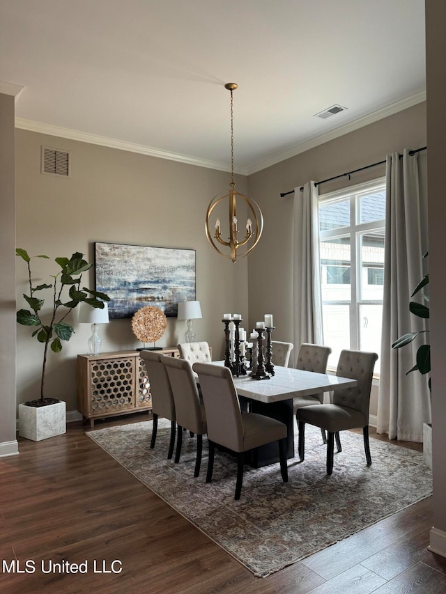 dining room with dark wood-type flooring, ornamental molding, and an inviting chandelier