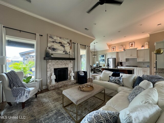 living room with crown molding, ceiling fan, a fireplace, and a wealth of natural light